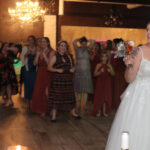 Bride looking back with flower bouquet, ready to toss the bouquet behind her to a crowd of girls gathered, as part of the "bouquet toss" tradition