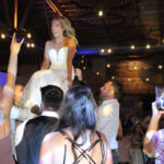 Bride held up on a chair in the middle of the dance floor, surrounded by people and hands in the air