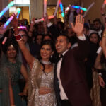 Bride and groom with friends and family behind them, with light sticks and hands in the air, having the best time with music and DJ services provided by Chicago area DJ company, Paul Michaels Events