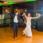 Bride and groom entering their reception with wide open arms.